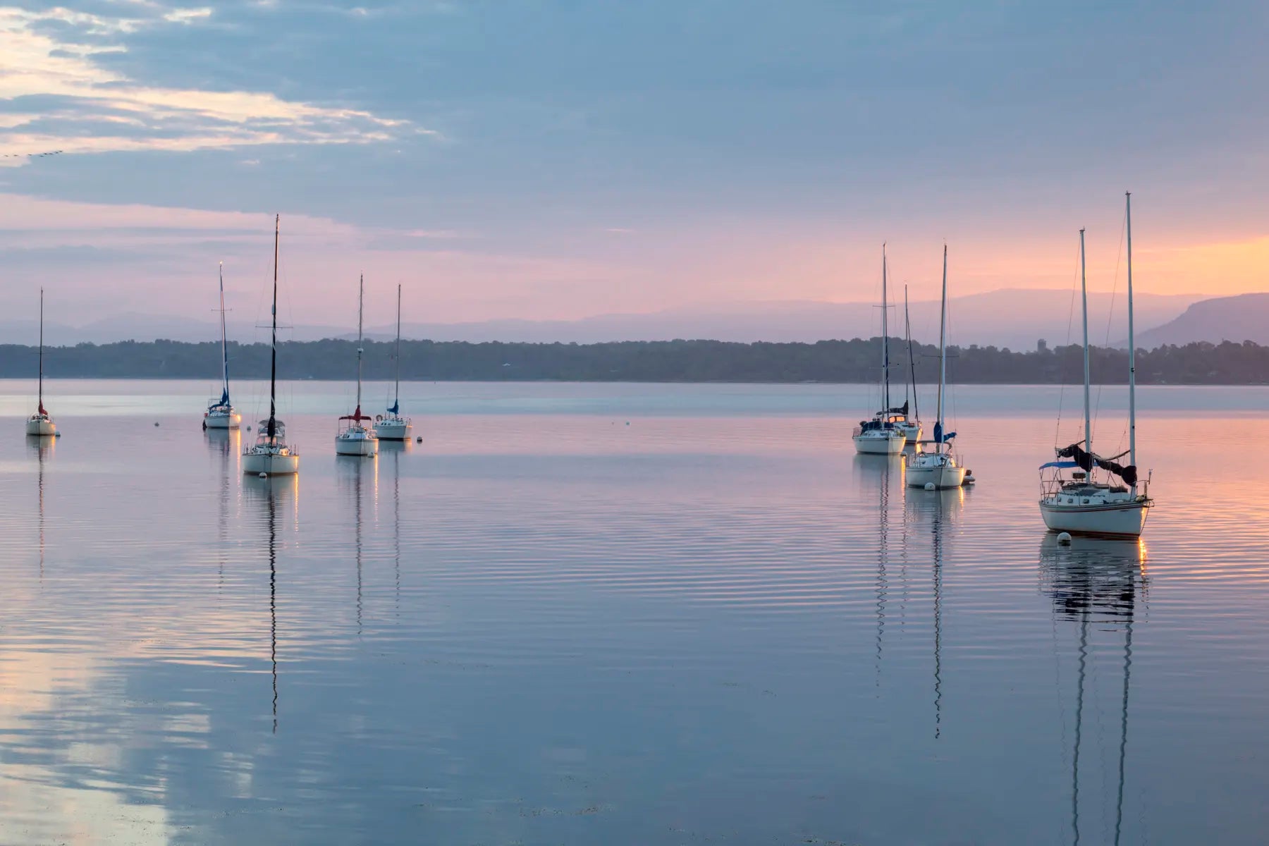 a pink sunrise over a flat lake with sailboats on moorings in the foreground