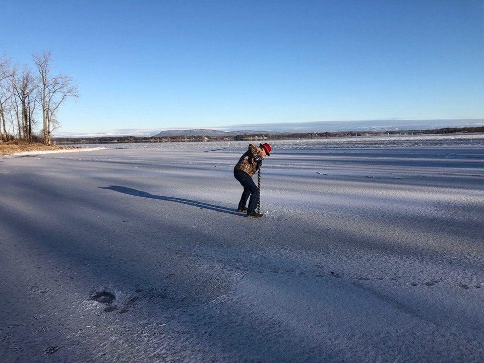 Person ice fishing on a frozen lake with a clear blue sky.