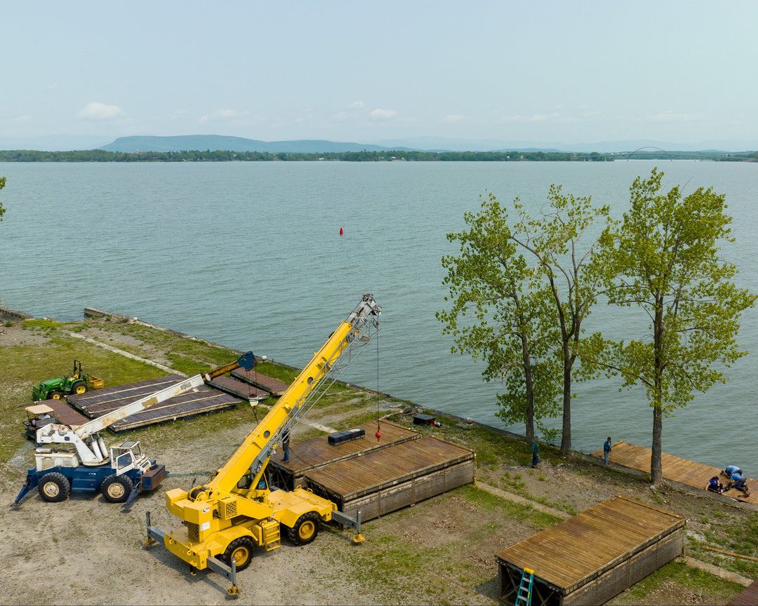 Two mobile cranes working on the shore of lake champlain.