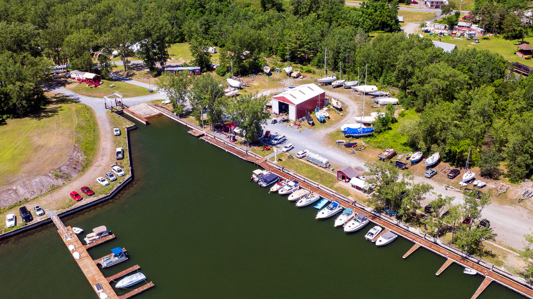 Aerial view of a marina with boats and docked cars near a forested area.